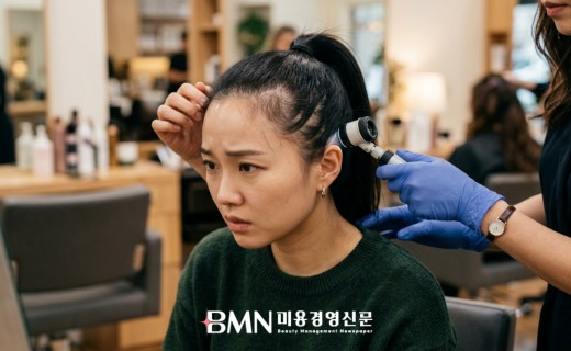 거울 앞에서 타이트하게 묶은 포니테일의 앞쪽 헤어라인을 들추며 가늘어진 모발을 걱정스럽게 확인하는 여성 고객