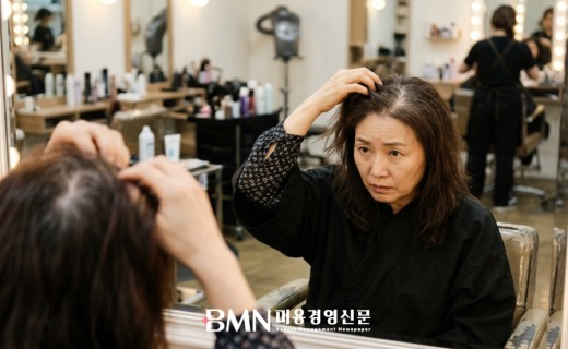 거울 앞에서 정수리 모발을 들어 올려 볼륨이 줄어든 상태를 확인하는 40대 여성 고객